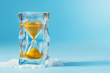 Hourglass in ice cube, frozen time. Stopping the time concept, freeze time, sand clock in ice, copy space. Climate change. Daylight saving time, save the date, fall back, spring forward.