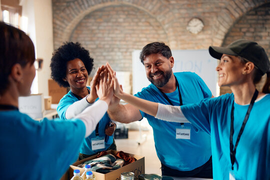 Group of happy volunteers gathering hands in unity while working at charitable foundation.