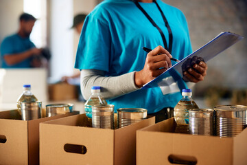Close up of black woman making list of donated groceries while volunteering at food bank.