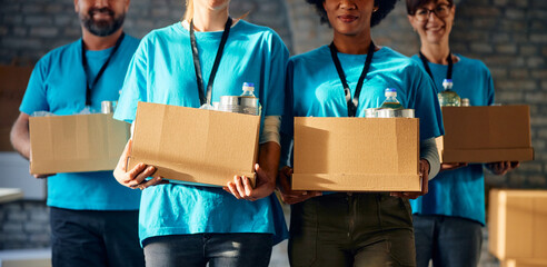 Unrecognizable team of volunteers carrying donation boxes at food bank.