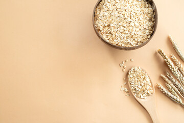 Oats or oat flakes in wooden bowl and golden wheat ears on beige background. Top view, horizontal. Healthy lifestyle, healthy nutrition, vegan food concept