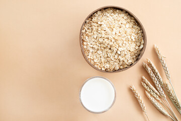 Oats or oat flakes in wooden bowl and golden wheat ears on beige background. Top view, horizontal. Healthy lifestyle, healthy nutrition, vegan food concept