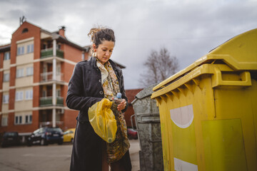 one woman stand with plastic garbage in front of recycle containers