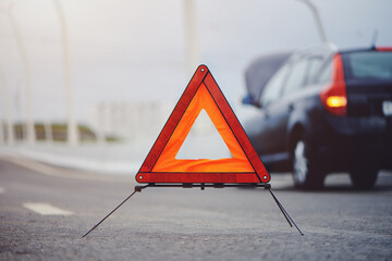 Close-up view of emergency stop sign on asphalt road, blurred background of emergency vehicle with hazard lights and raised hood.