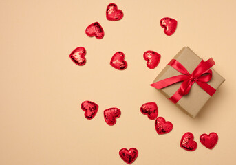 Box tied with a red ribbon and small hearts on a beige background, top view