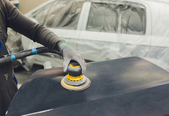 Auto mechanic preparing the car for paint job by applying polish with the power buffer machine