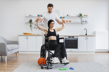 Trainer or husband helping mature woman in wheelchair lifting arms with dumbbells for muscle strength in rehabilitation. Physiotherapy healthcare, medical doctor consulting disabled caucasian patient.