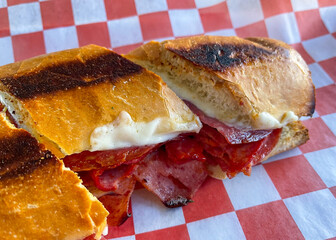 Grilled sandwich with Italian meats on red and white checkered wax paper