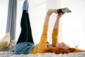 Funny young woman doing acrobatics in her bedroom and taking selfies with her digital tablet....