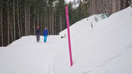 Fotobehang Tourist Couple Passing By Hiking Trail Marker Pole in Austrian Alps During Snow Blizzard on Winter Day © rohawk