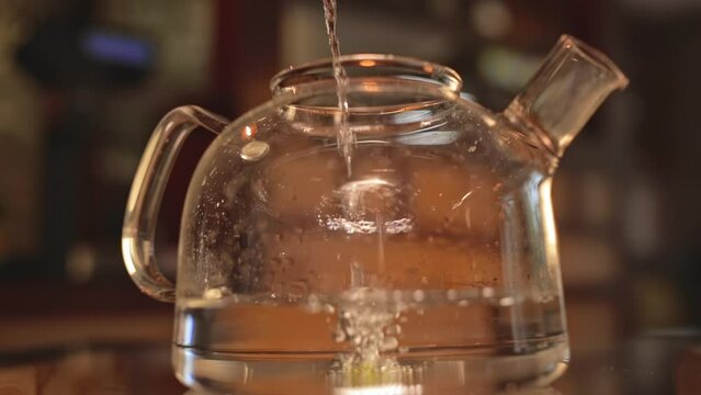 A stream of water pours into a large clear teapot