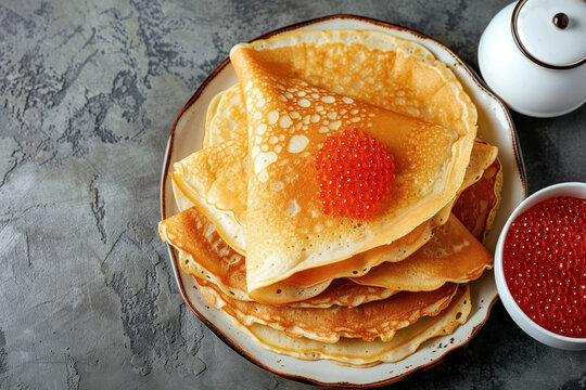 Several of thin pancakes decorated with red caviar on white plate flat lay on grey concrete background with copy space, festive dish for maslenitsa week