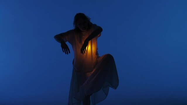 Female dancer performing in the studio. Young woman dancing in dark studio with warm light glowing inside the chest under her shirt. Full shot 30 fps