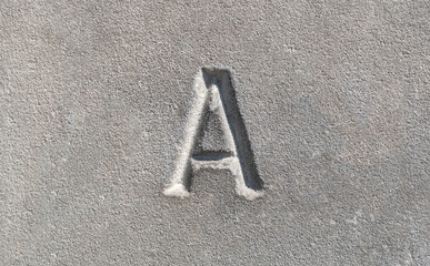 Close-up view of a single one letter A carved into a smooth gray stone. Latin alphabet letters,...