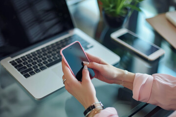 A woman holding a cell phone in front of a laptop