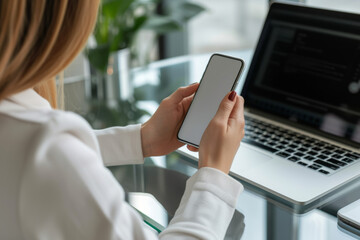 A woman is holding a cell phone in front of a laptop