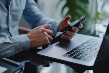 A man is using a cell phone next to a laptop