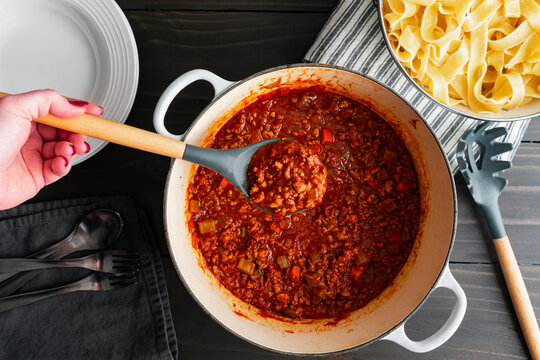 Hand Holding a Serving Spoon of Authentic Bolognese Sauce: Ragu alla bolognese Italian tomato and meat sauce in a spoon held over a large pot