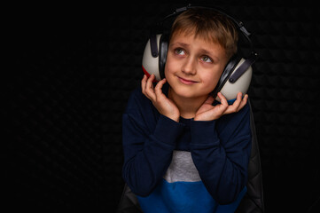 portrait of smiling fair haired teenage boy in blue with headphones looking up hearing test. in a...