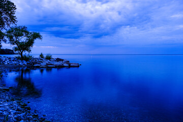 Summer blue Lake Ontario just after sunset with tree and stone shore
