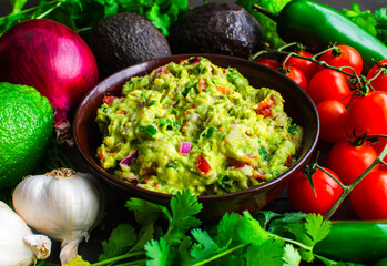 Bowl of Guacamole Surrounded by Fresh Ingredients: Guacamole with Hass avocados, jalapeno peppers, cherry tomatoes, and other ingredients
