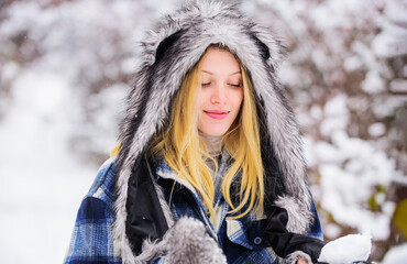 Wintertime. Blonde woman in plaid coat, fur hat and mittens with snowball in hands. Winter...