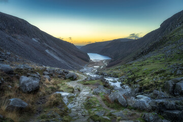 Stone path, trail with a scenic view on Glendalough Lake, stream and valley. Hiking in Wicklow Mountains at sunset, Ireland