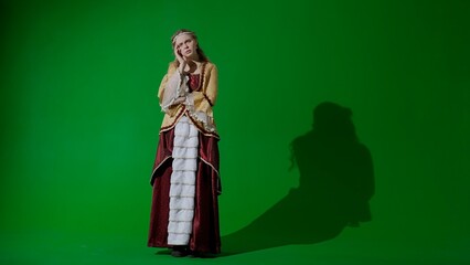 Woman in ancient outfit on the chroma key green screen background. Female in renaissance style dress posing looking at the camera, sad face.