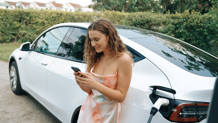 Young woman use smartphone to pay for electricity at public EV car charging station in nature....