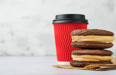 A stack of chocolate brownies on a plate and coffee in a red craft takeaway glass on a light background. Horizontal, free space for copying..