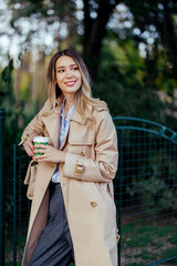 Woman drinking coffee to go outside and leaning on a fence.