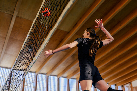 A young volleyball player is jumping and hitting a ball over the net.