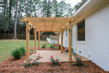 The rear back exterior of a newly painted and renovated white brick ranch style house with a large yard and a newly built wood arbor pergola for shade