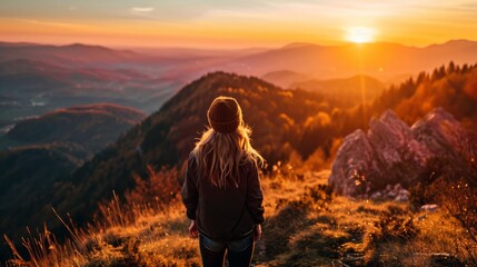 Fototapeta premium woman from behind, on the top of a mountain, enjoying a sunset generative ai
