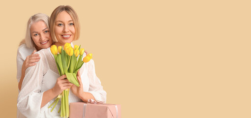 Woman and her adult daughter with flowers and gift on beige background with space for text. Banner...