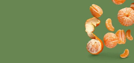Peeled flying tangerines on green background with space for text