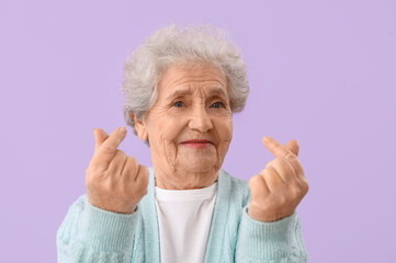 Senior woman making heart with her fingers on lilac background, closeup