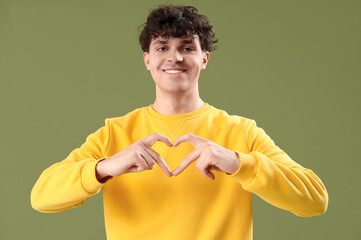 Handsome young man making heart with his hands on green background