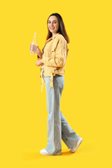 Young woman with bottle of water on yellow background