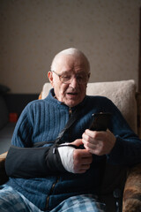 Senior with injured arm in sling browsing smartphone.