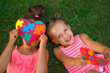 Funny happy girls are lying on the grass playing with heart-shaped postcards with glued pieces of...