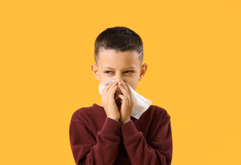 Ill little boy with tissue sneezing on yellow background