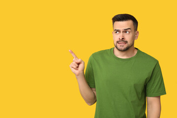 Handsome ashamed young man pointing at something on yellow background