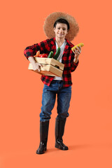 Little farmer holding wooden box with different vegetables on orange background
