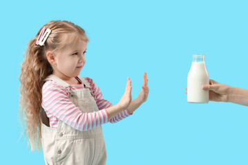 Cute little girl rejecting bottle of milk on blue background