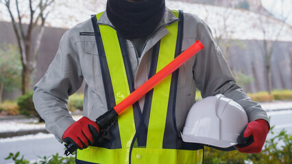 ネックウォーマーで防寒対策｜誘導灯を持つ誘導員と積雪風景