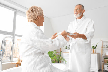 Mature woman taking clean towel from her husband in bathroom