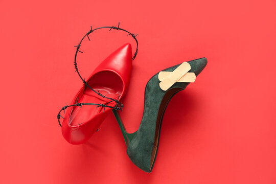 High-heeled shoes with plasters and barbed wire on red background. Uncomfortable shoes concept