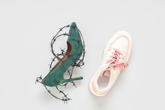 High-heeled sneaker and shoe wrapped in barbed wire on white background. Uncomfortable shoes concept