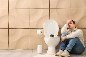 Young man and toilet bowl with cactus in restroom. Hemorrhoids concept